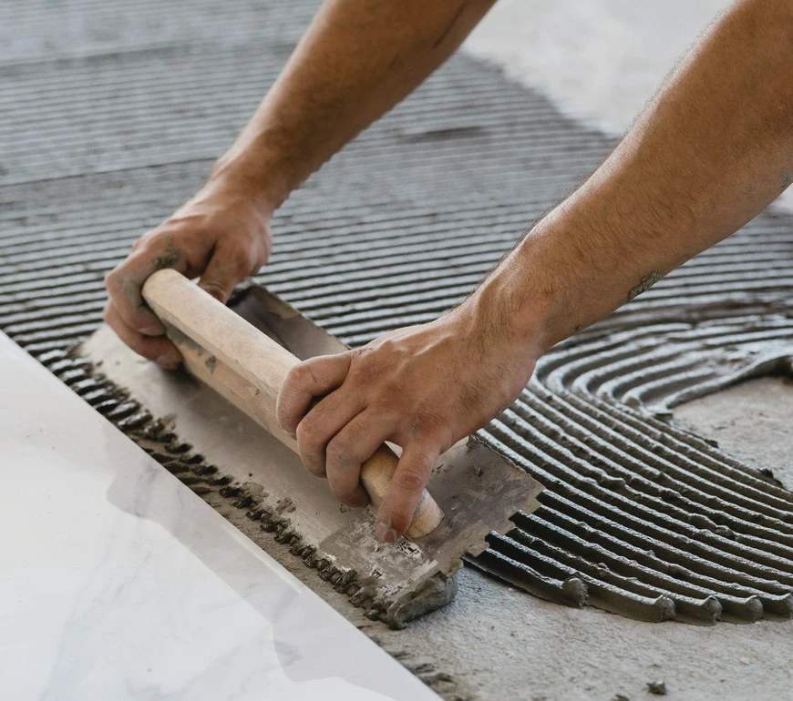 Rozprowadzanie kleju na&nbsp;podłożu za&nbsp;pomocą pacy zębatej podczas przygotowania podłoża pod&nbsp;płytki